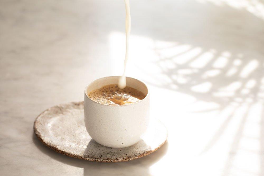Oat milk beside a coffee cup